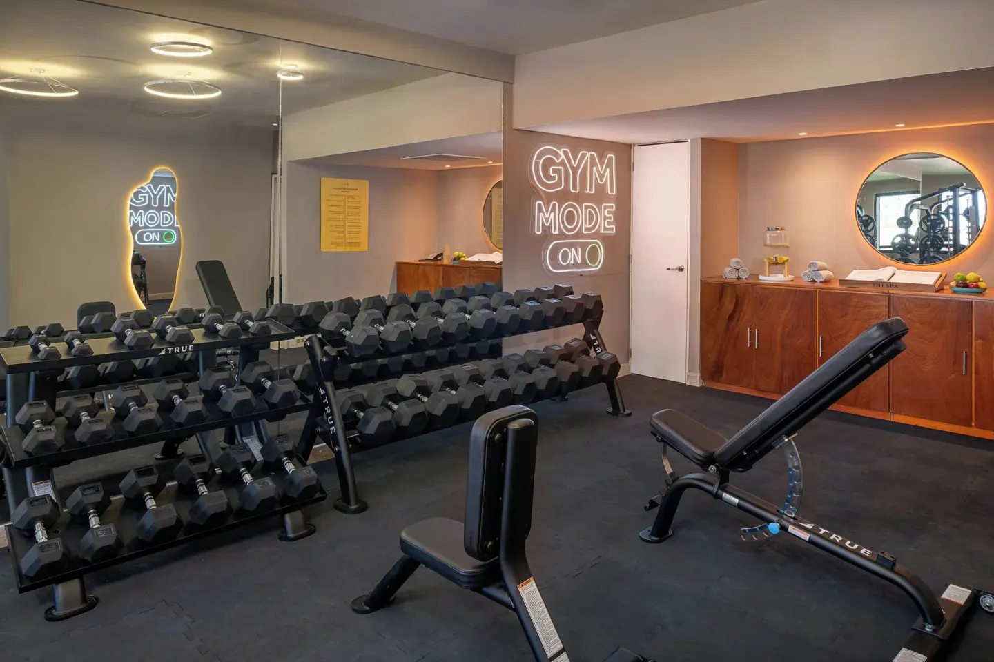Dumbbell racks, benches, mirrors, and a neon gym sign at Melia Casa Maya Cancun.