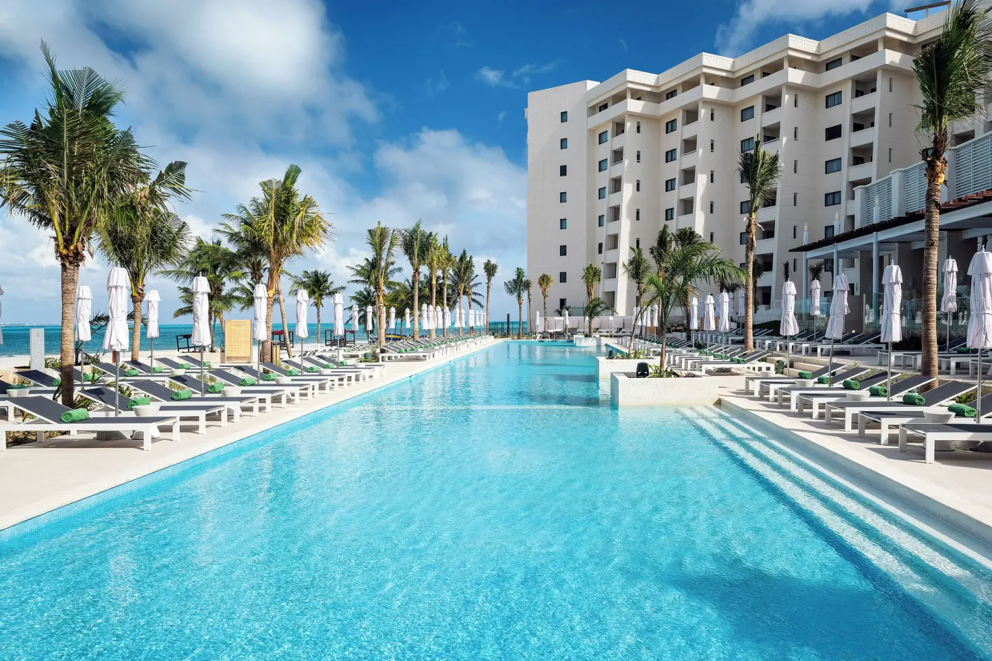 Sunlit pool flanked by palm trees and loungers at Melia Casa Maya Cancun.