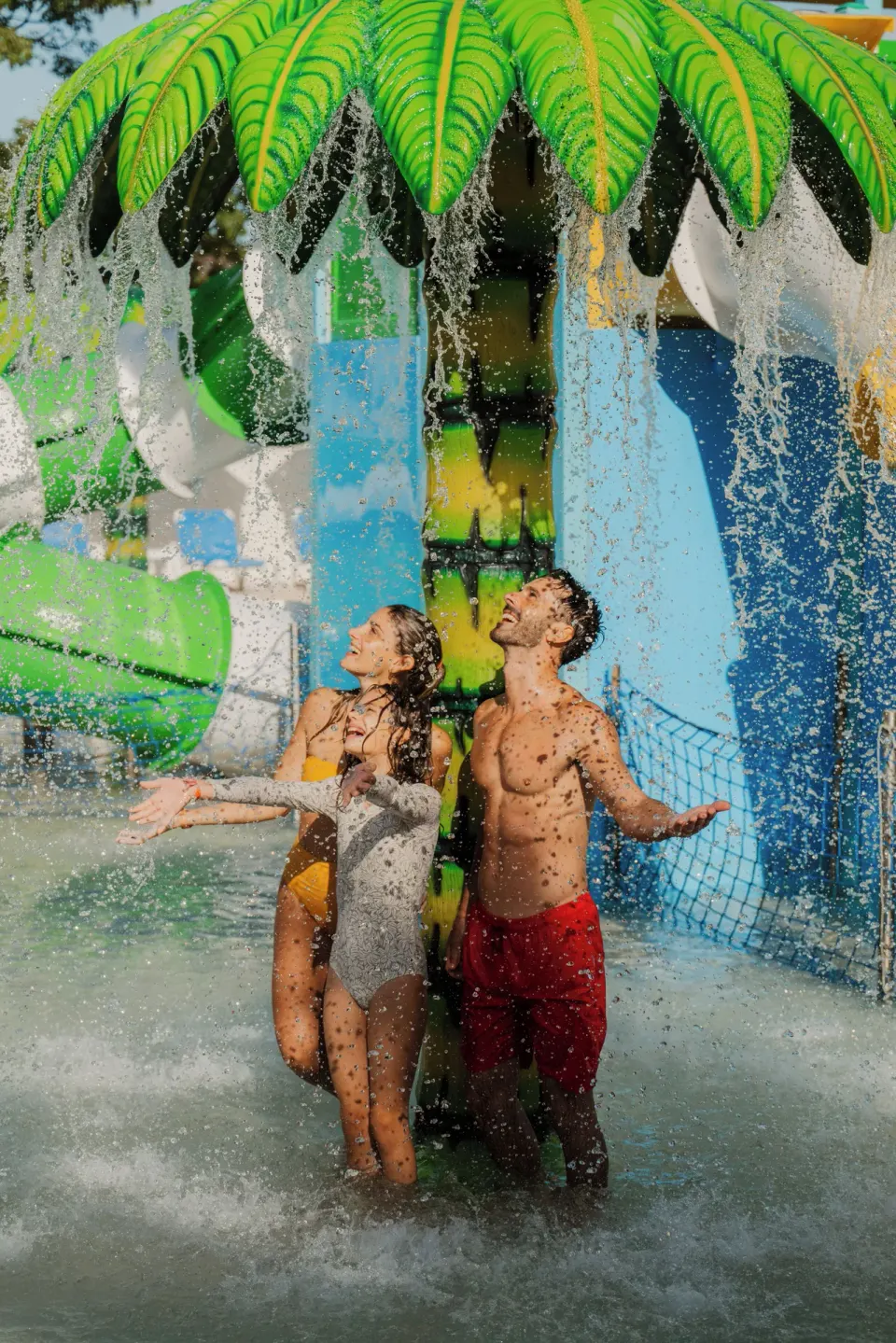 Two guests stand under a palm-shaped water spray in the splash area at Melia Casa Maya Cancun.