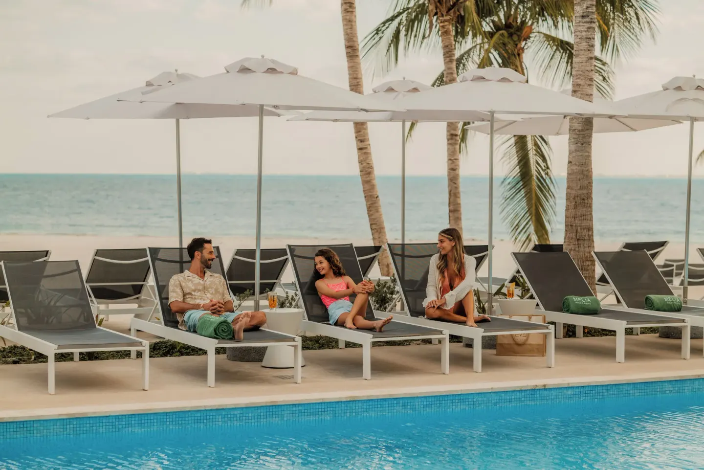 Guests lounging on poolside chairs under white umbrellas at Melia Casa Maya Cancun.