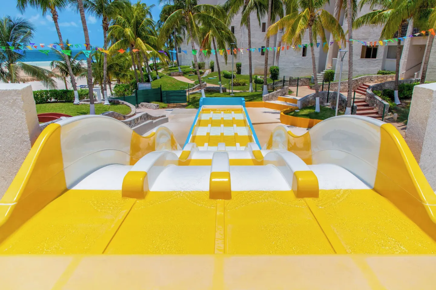 Top view down a yellow multi-lane water slide toward palms and the beach at Melia Casa Maya Cancun.