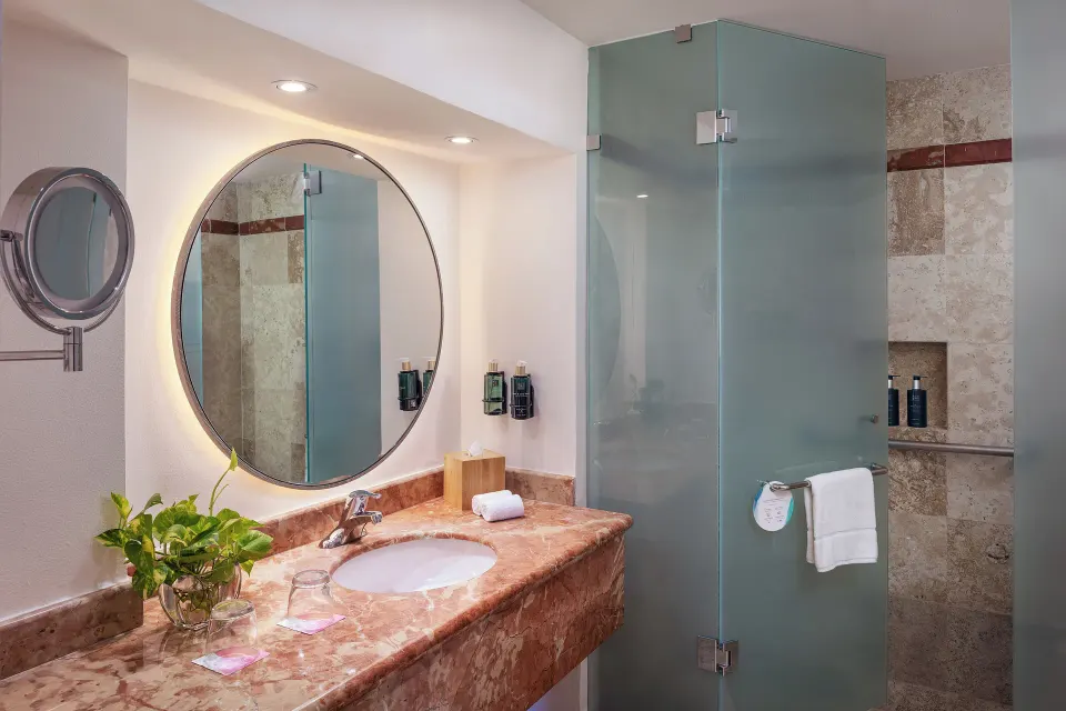 The Level Grand Suite bathroom with marble vanity, round mirror, and glass shower at Melia Casa Maya Cancun.