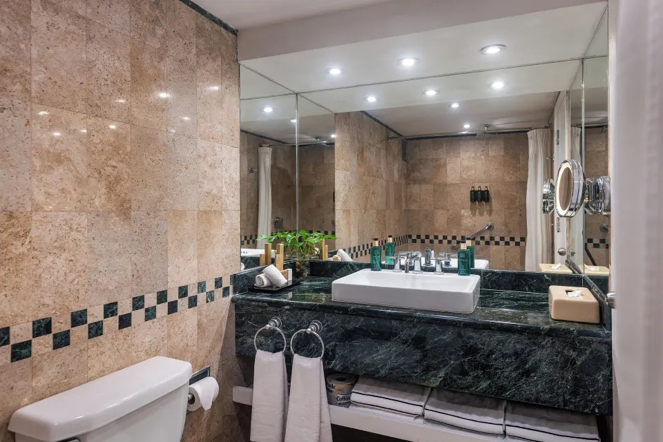 Bathroom sink and mirror with green-marble countertop and folded towels at Melia Cozumel