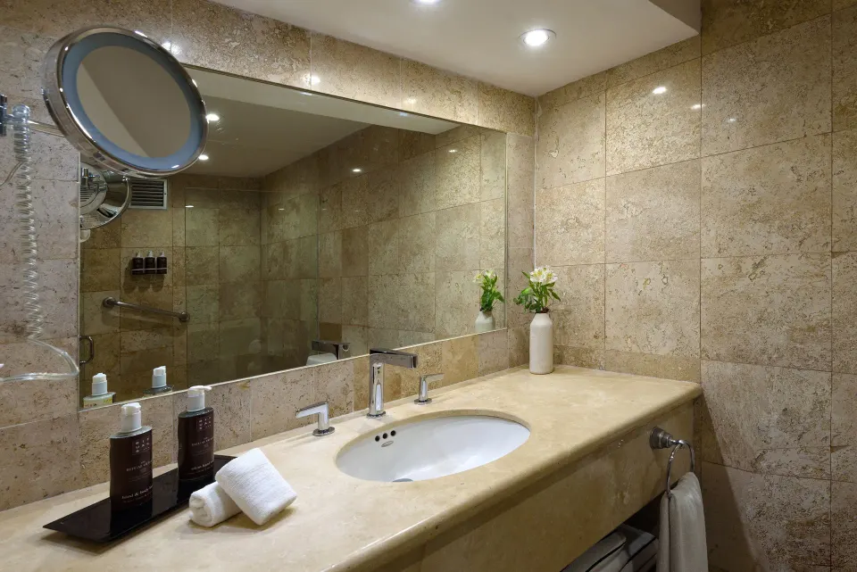 Vanity and sink area with large mirror in a marble-tiled bathroom at Melia Cozumel