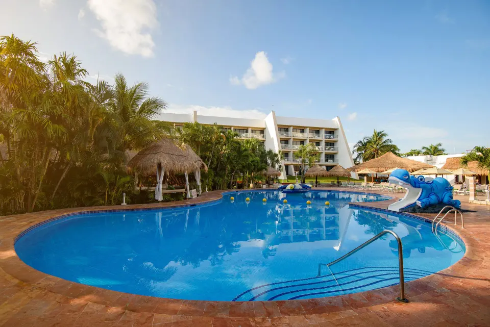 Resort pool with water slide, thatched cabanas and hotel building at Melia Cozumel