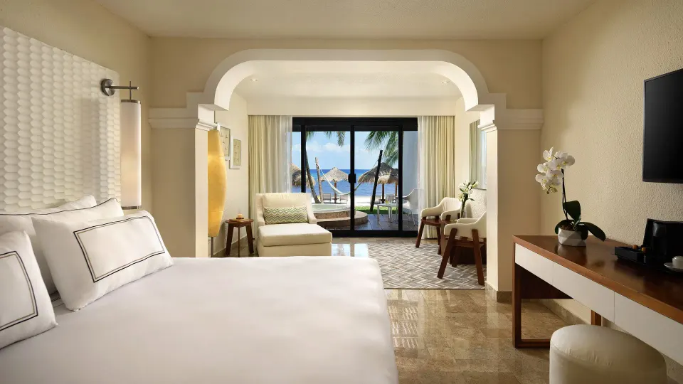 King bed and seating area with balcony view of palm trees and ocean at Melia Cozumel