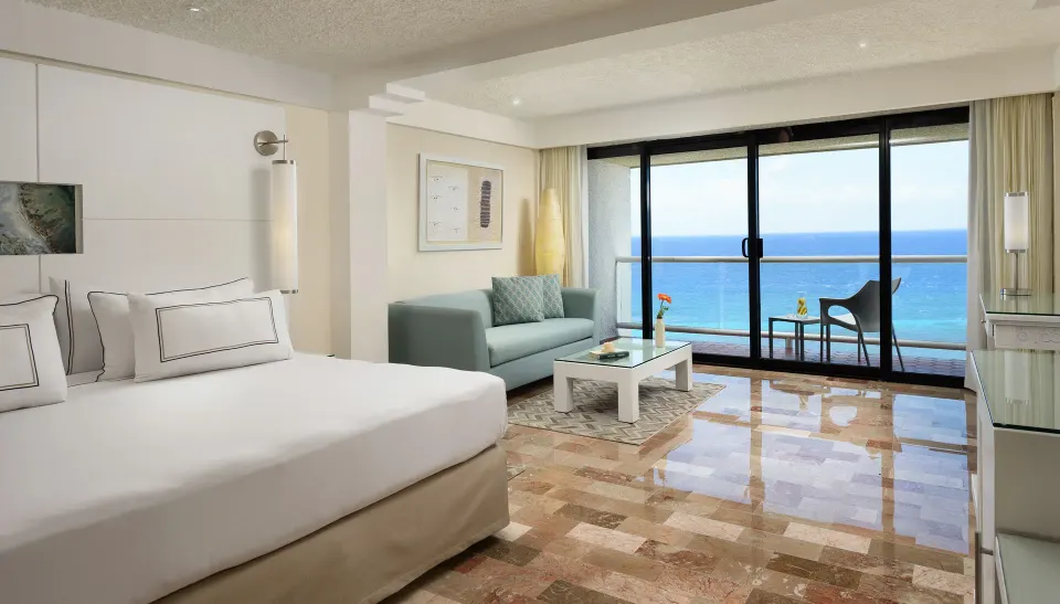 Spacious junior suite with king bed, seating area and balcony overlooking the ocean at Melia Cozumel