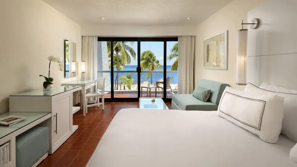 Junior suite with king bed, desk, sofa and balcony framed by palm trees at Melia Cozumel