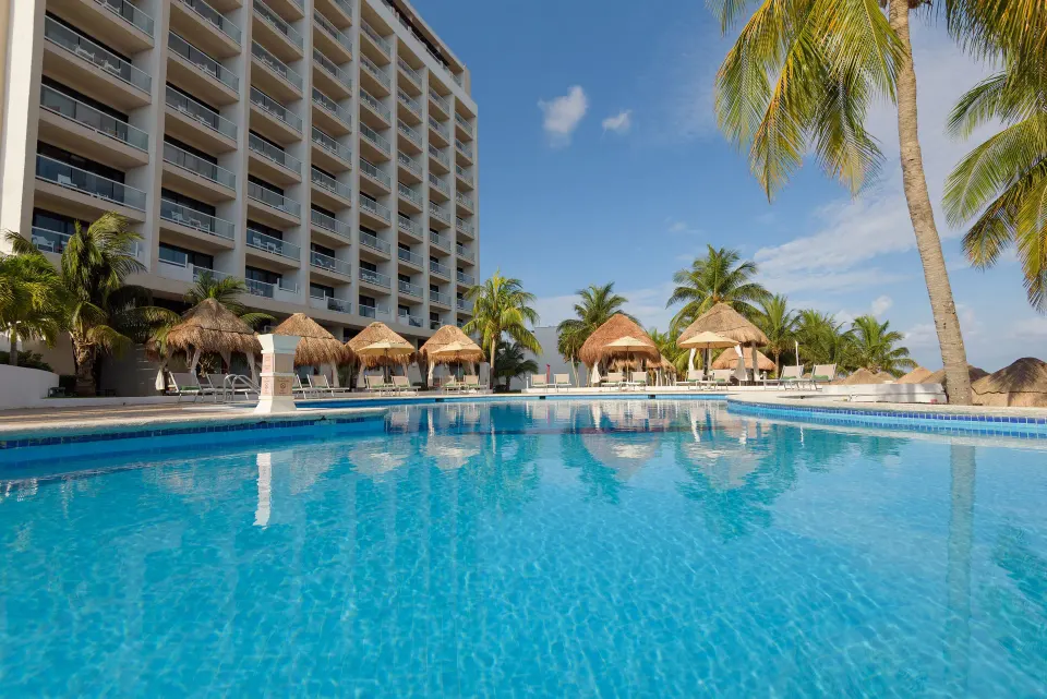 Large pool with hotel tower and shaded palapas in the background at Melia Cozumel