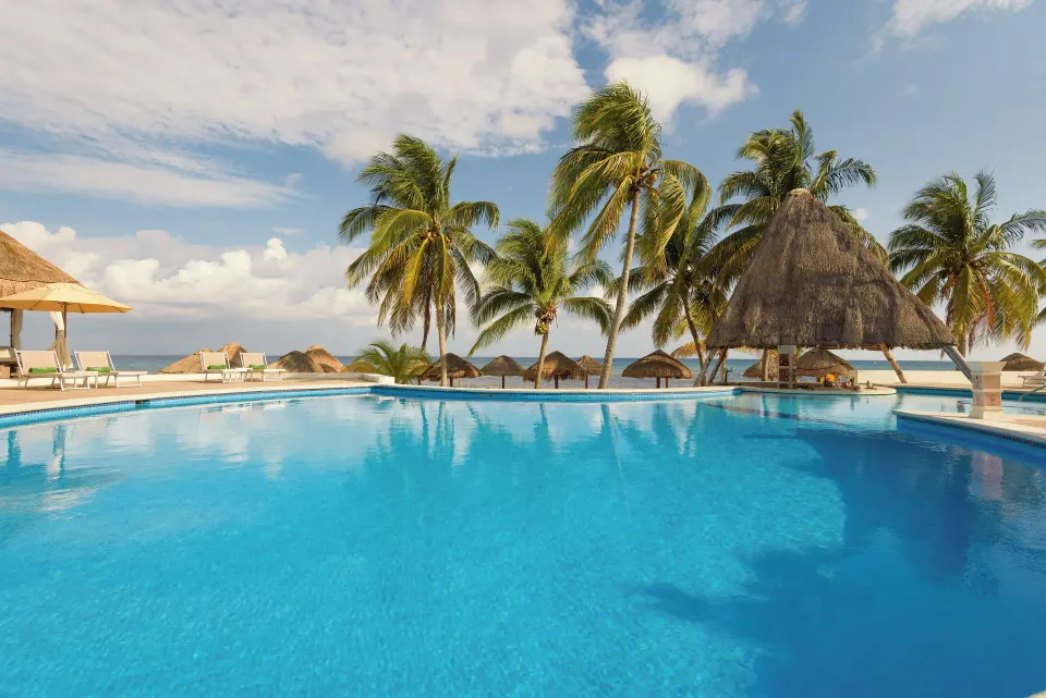 Pool close-up with palms and palapa cabana overlooking the ocean at Melia Cozumel