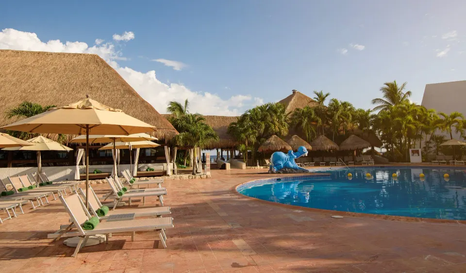 Pool deck with loungers, umbrellas and palapas beside the pool at Melia Cozumel