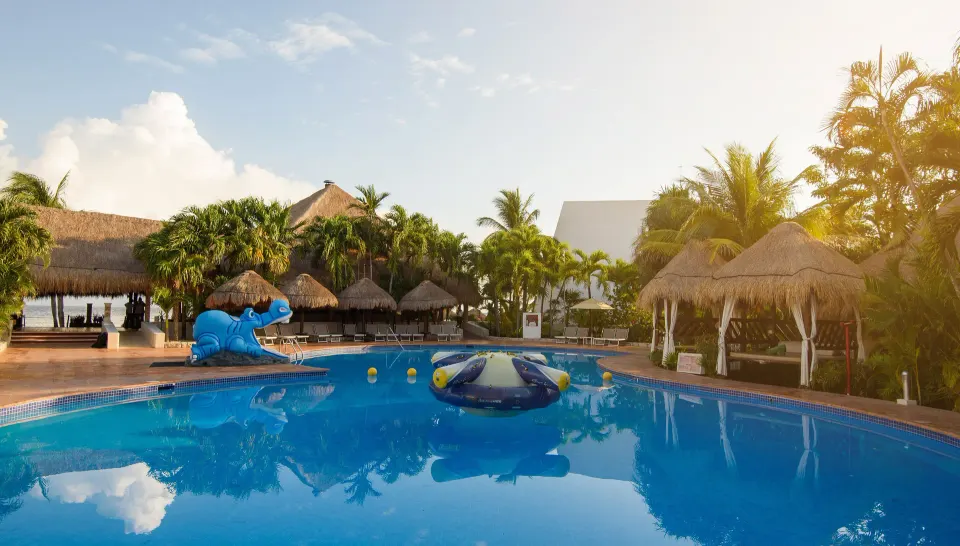 Pool with inflatable play ring and blue slide among palm trees at Melia Cozumel