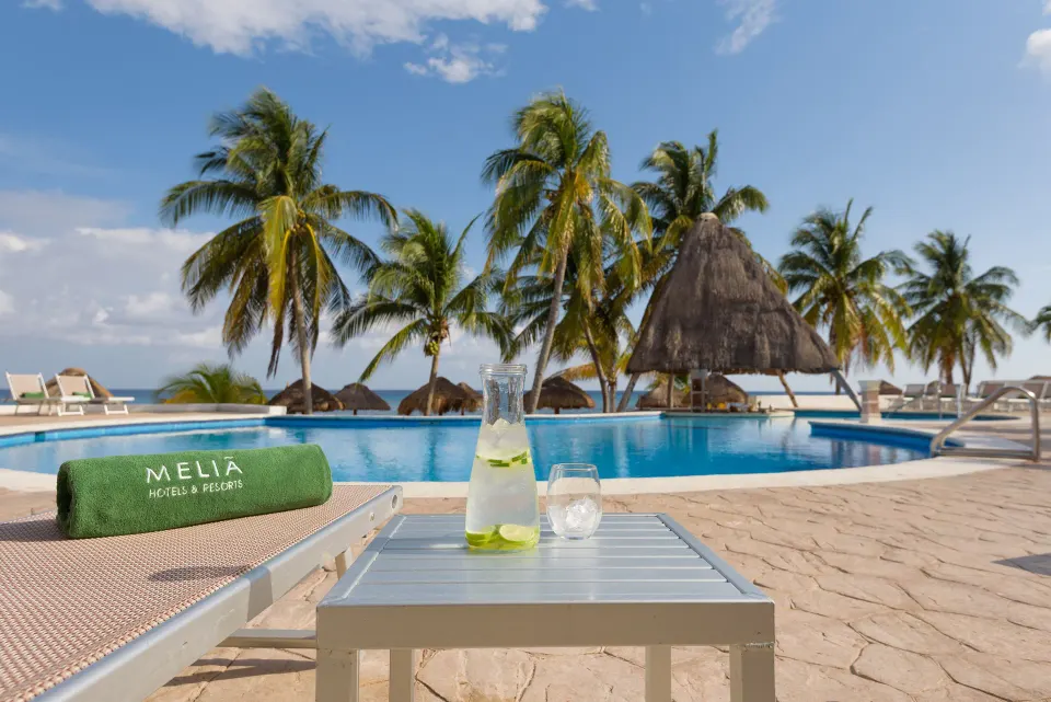 Poolside lounger with green towel and pitcher of lime water overlooking the pool at Melia Cozumel