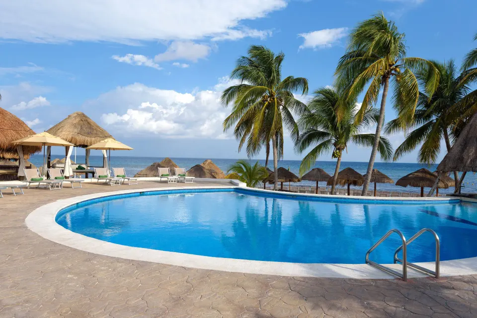 Resort swimming pool with loungers, palapas and ocean beyond at Melia Cozumel