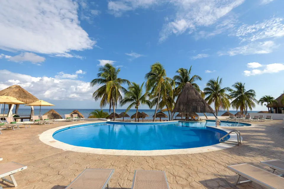 Round seaside pool with palm trees and palapa umbrellas at Melia Cozumel