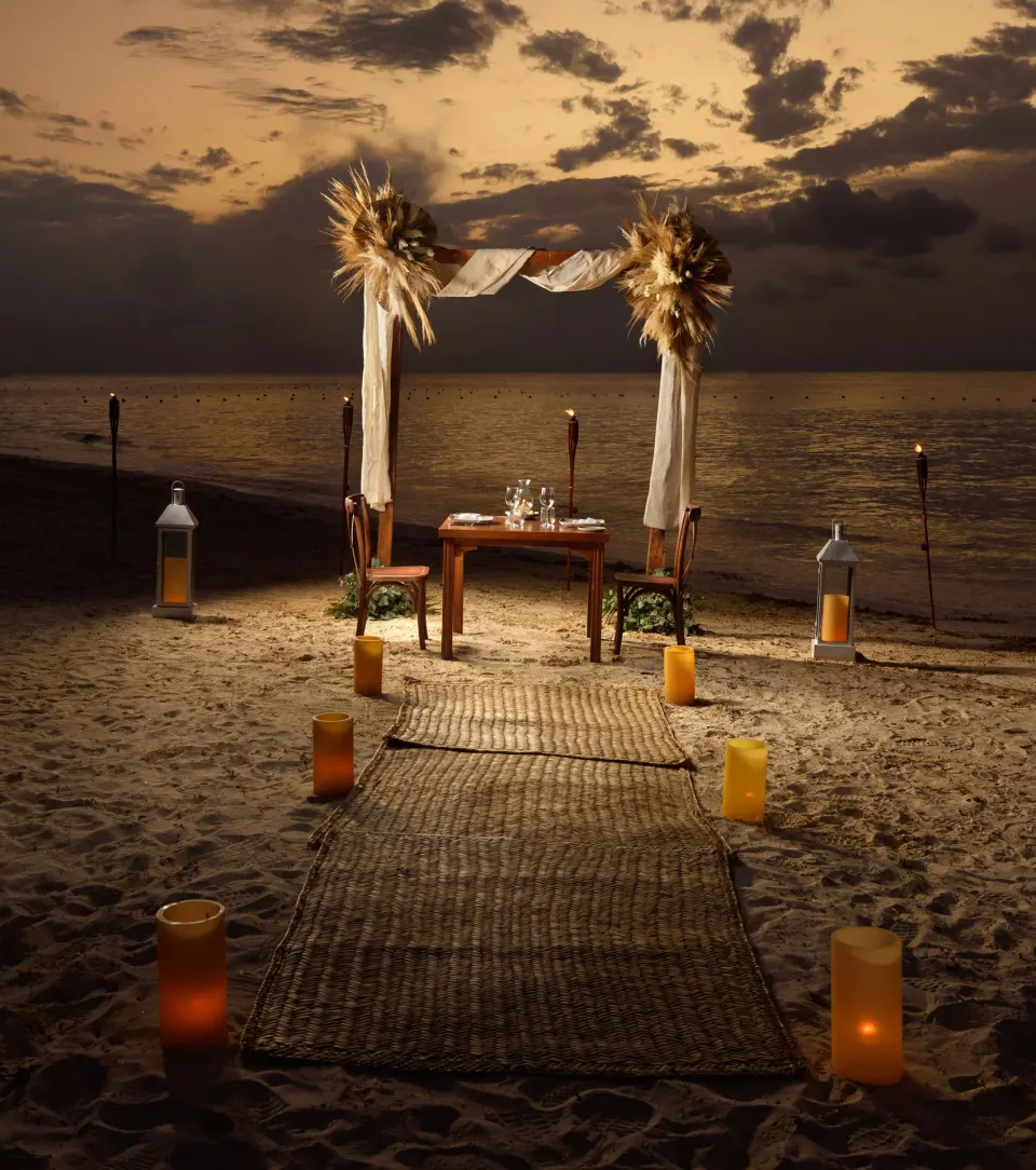 Candlelit dinner table under a framed arch on the sand at Melia Cozumel