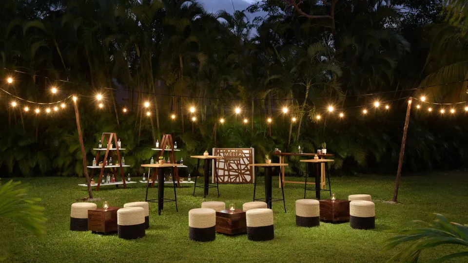 Lawn setup with string lights, stools and high tables for an outdoor event at Melia Cozumel