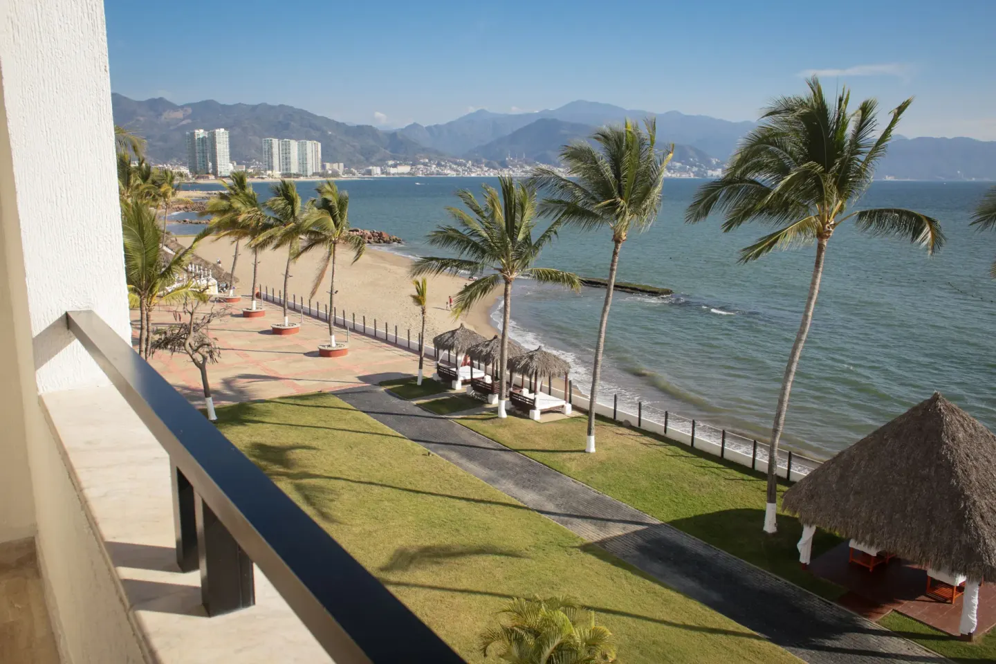 Balcony view of palm trees, beach, palapas, bay, and mountains at Melia Puerto Vallarta.