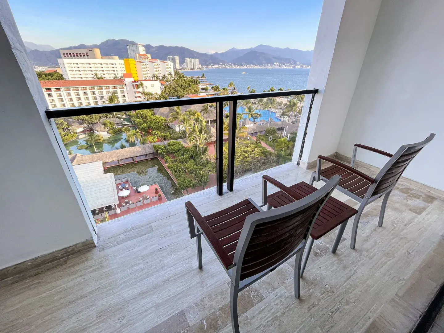 Balcony with two chairs overlooking resort grounds, pools, bay, and mountains at Melia Puerto Vallarta.