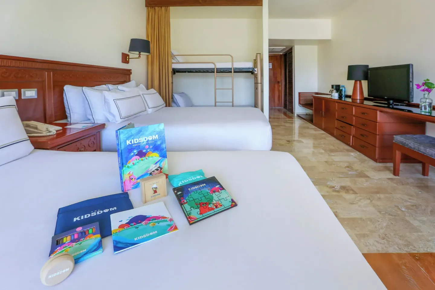 Family guest room with two beds, bunks, TV, and kids’ activity items at Melia Puerto Vallarta.