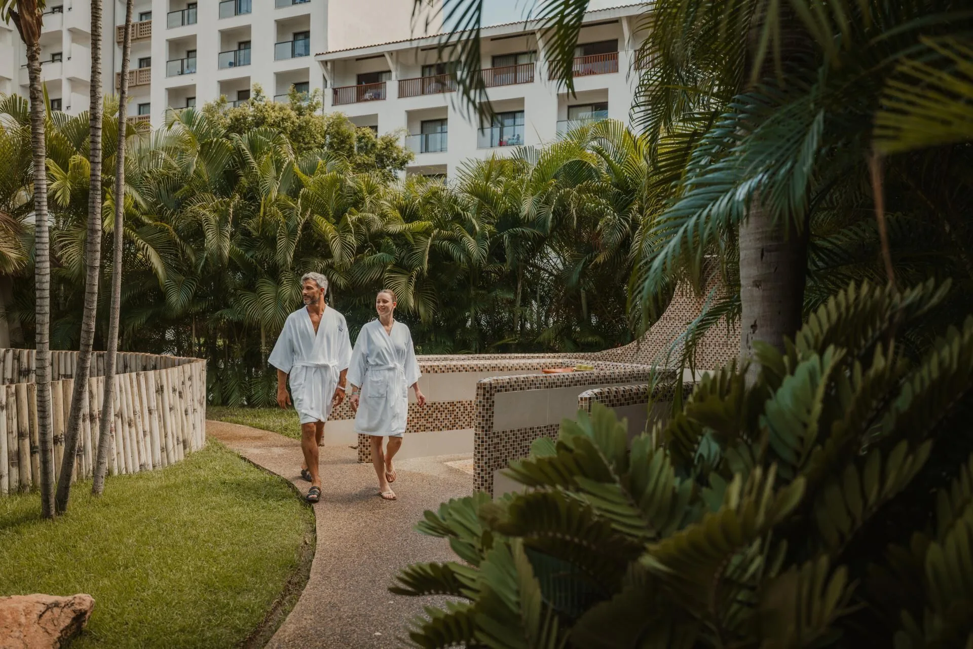 Guests in robes walk through tropical gardens at Melia Puerto Vallarta.