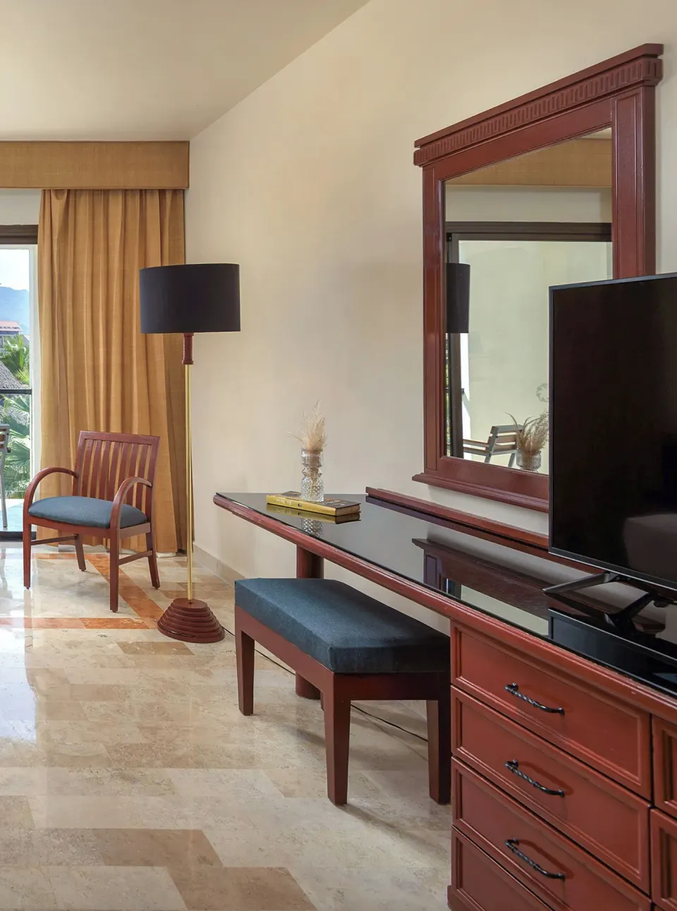 Guest room dresser, mirror, TV, chair, and balcony door at Melia Puerto Vallarta.