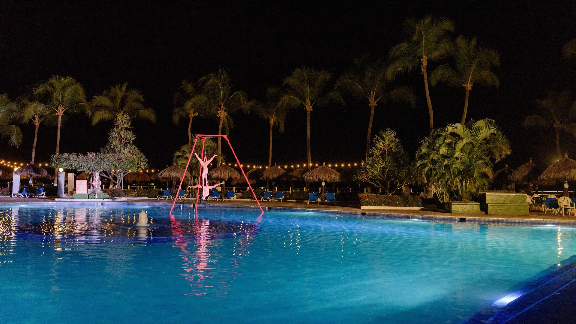 Wide night view of the pool, acrobats, palms, and lounge chairs at Melia Puerto Vallarta.