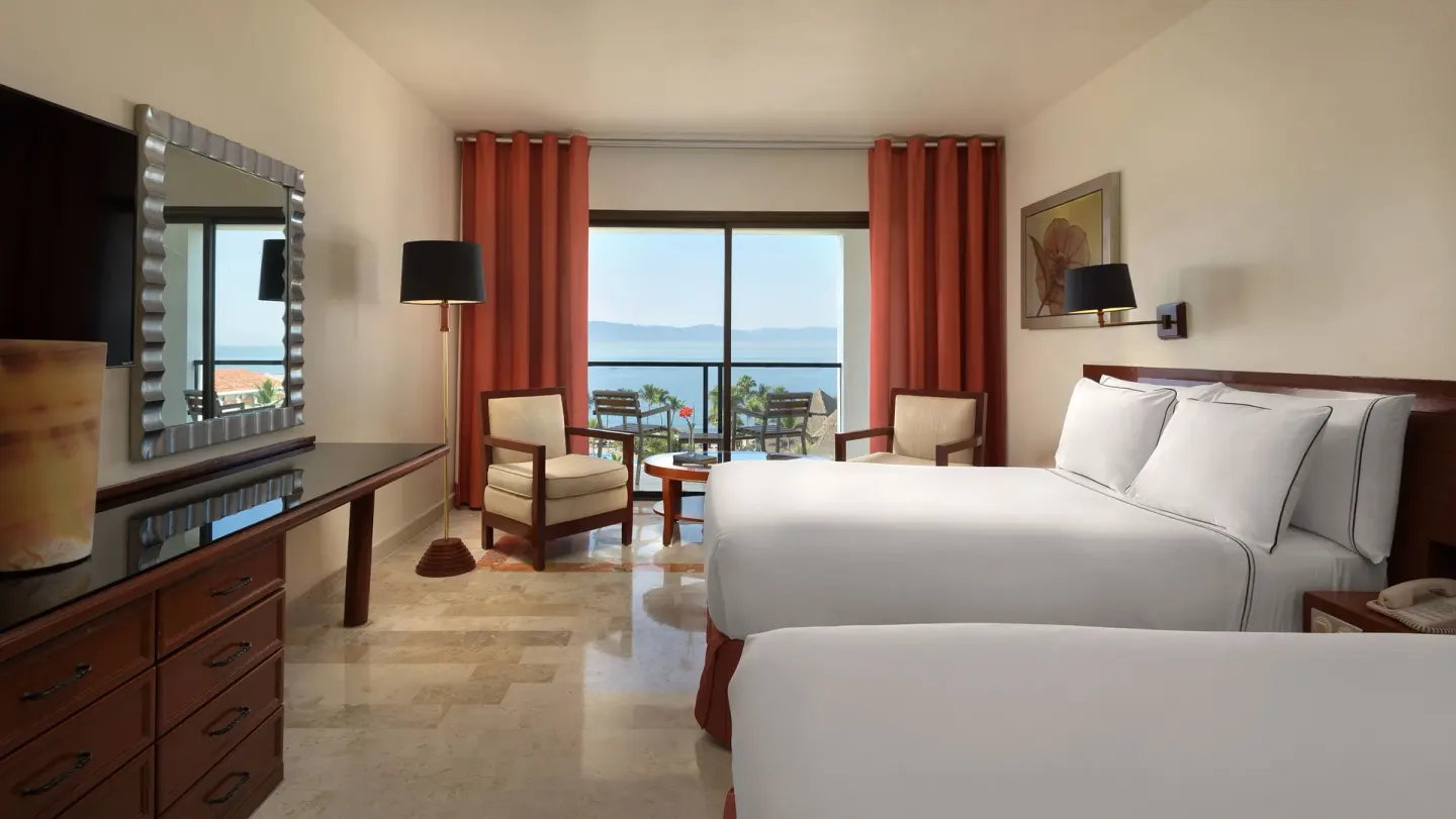 Guest room with two beds, seating, and ocean-view balcony at Melia Puerto Vallarta.