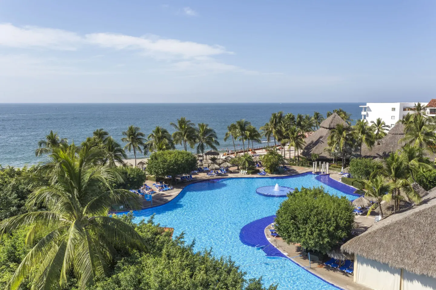 Oceanfront pool with palms and thatched roofs at Melia Puerto Vallarta.