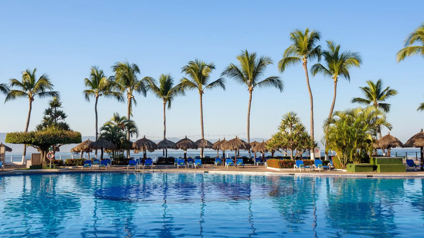 Pool deck lined with palms, palapas, and blue lounge chairs at Melia Puerto Vallarta.
