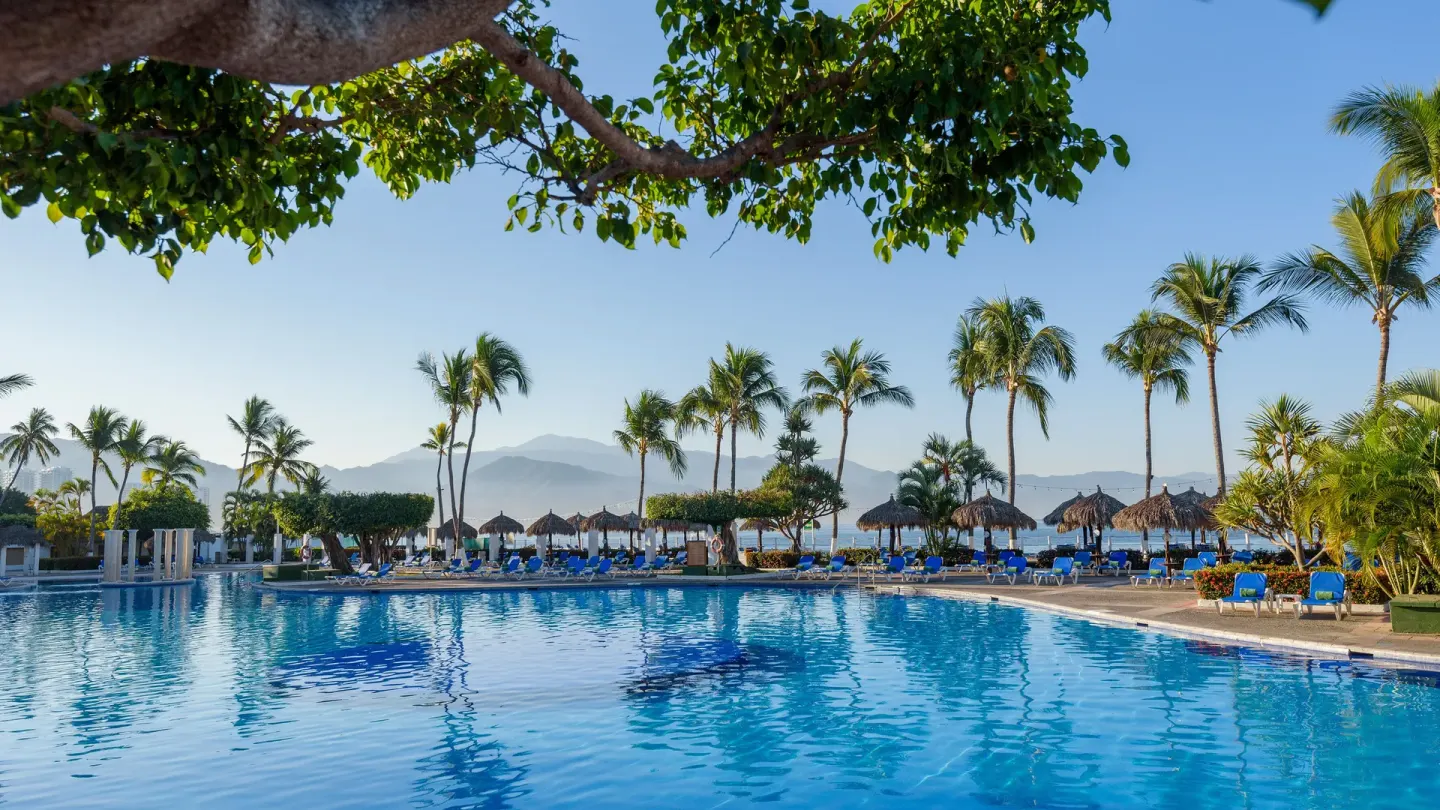Pool with palm trees, blue loungers, palapas, and bay views at Melia Puerto Vallarta.