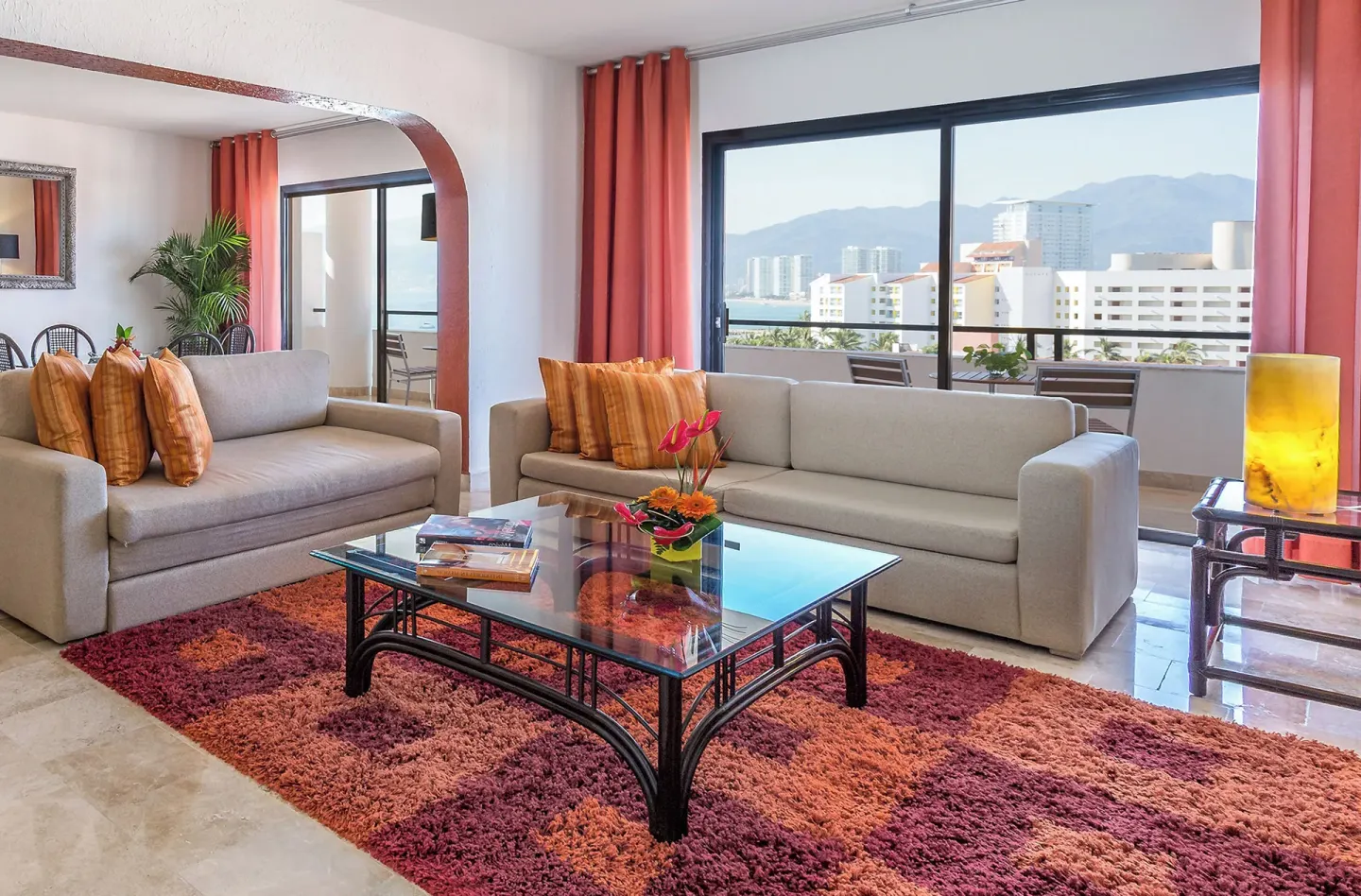 Suite living room with sofas, glass coffee table, balcony, and bay view at Melia Puerto Vallarta.