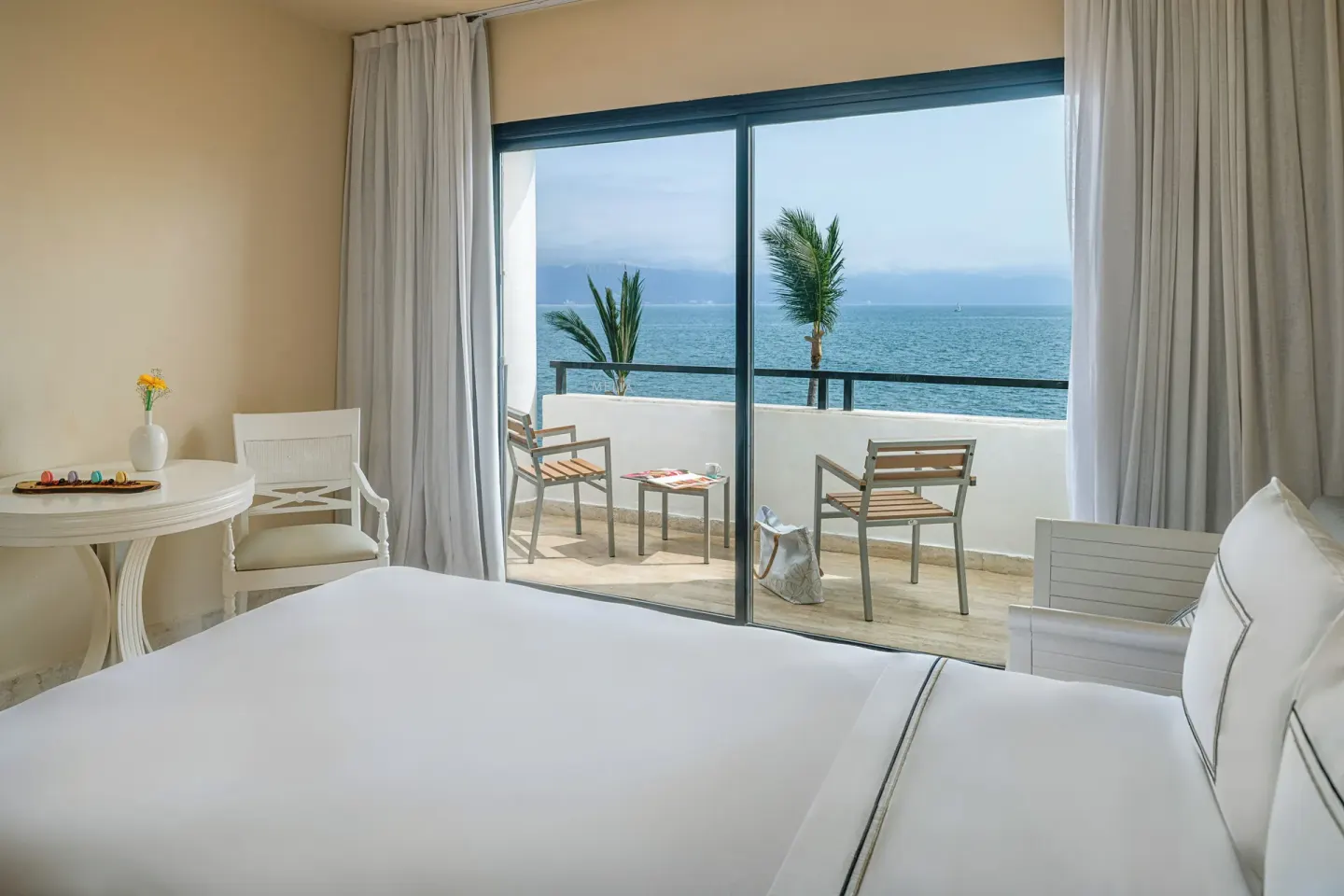 Premium Ocean Front bed beside sliding doors to a furnished ocean-view balcony at Melia Puerto Vallarta.