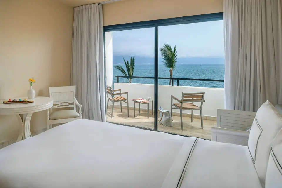 Premium Ocean Front bed beside sliding doors to a furnished ocean-view balcony at Melia Puerto Vallarta.
