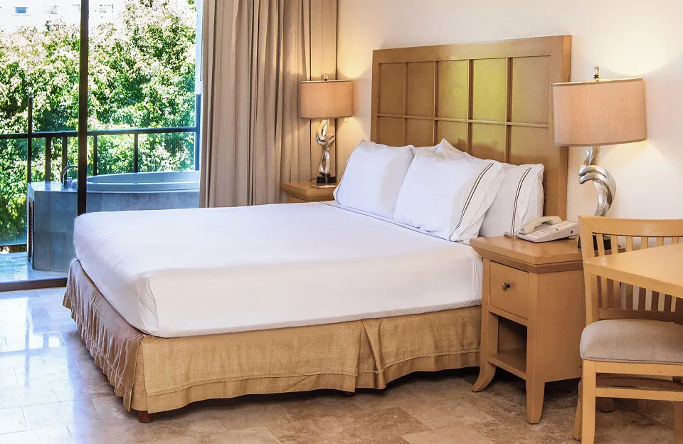 Premium Suite Garden View king bed beside balcony doors at Melia Puerto Vallarta.