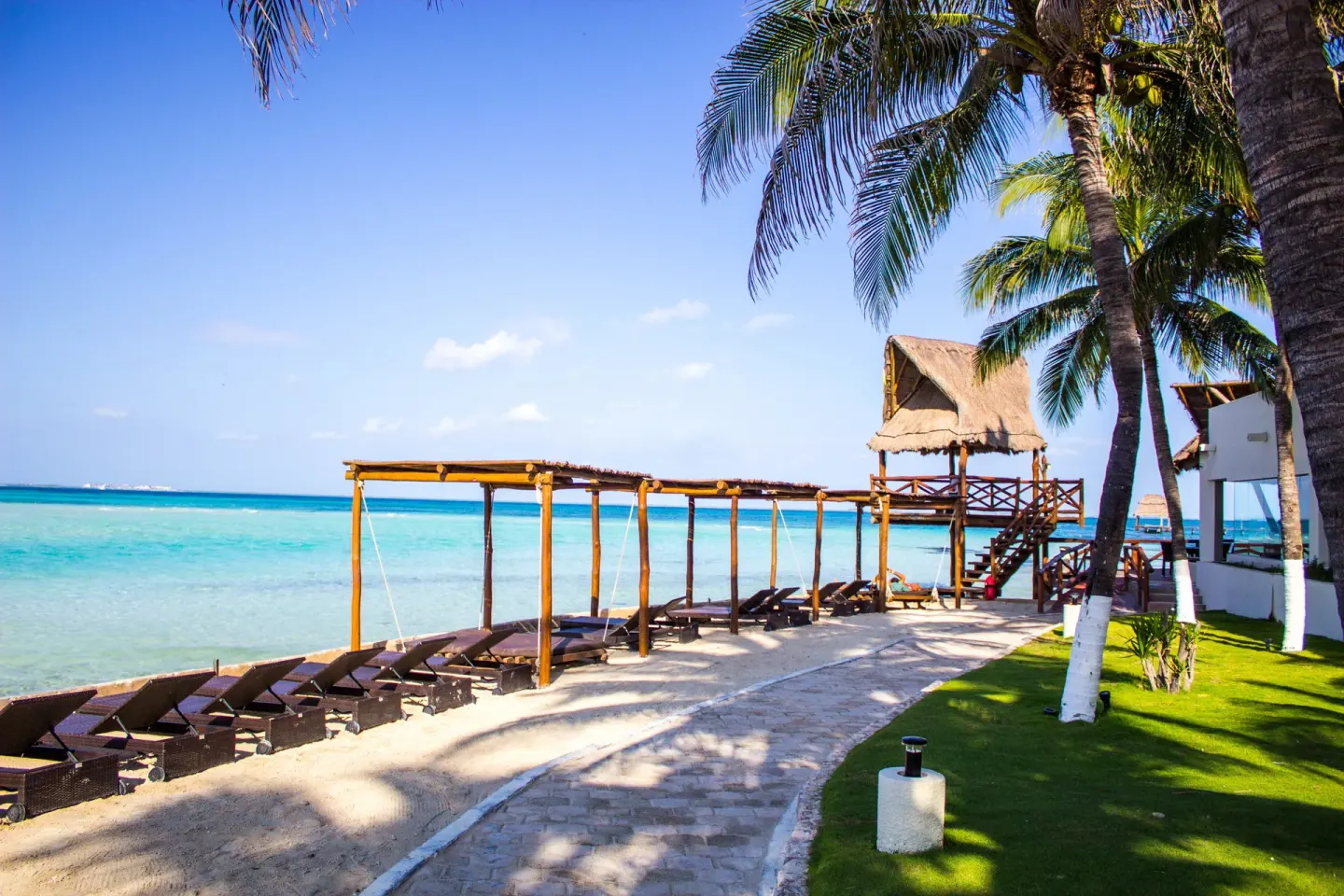 Beach loungers under shade structures beside palm trees at Mia Reef Isla Mujeres.