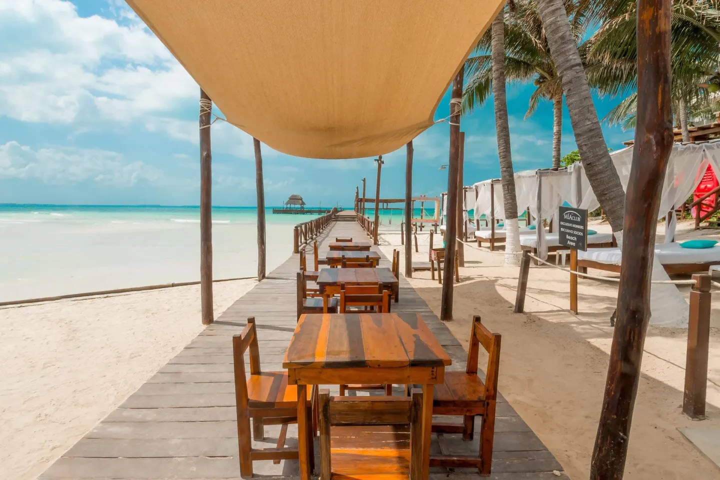 Shaded wooden beach walkway with tables and cabanas at Mia Reef Isla Mujeres.