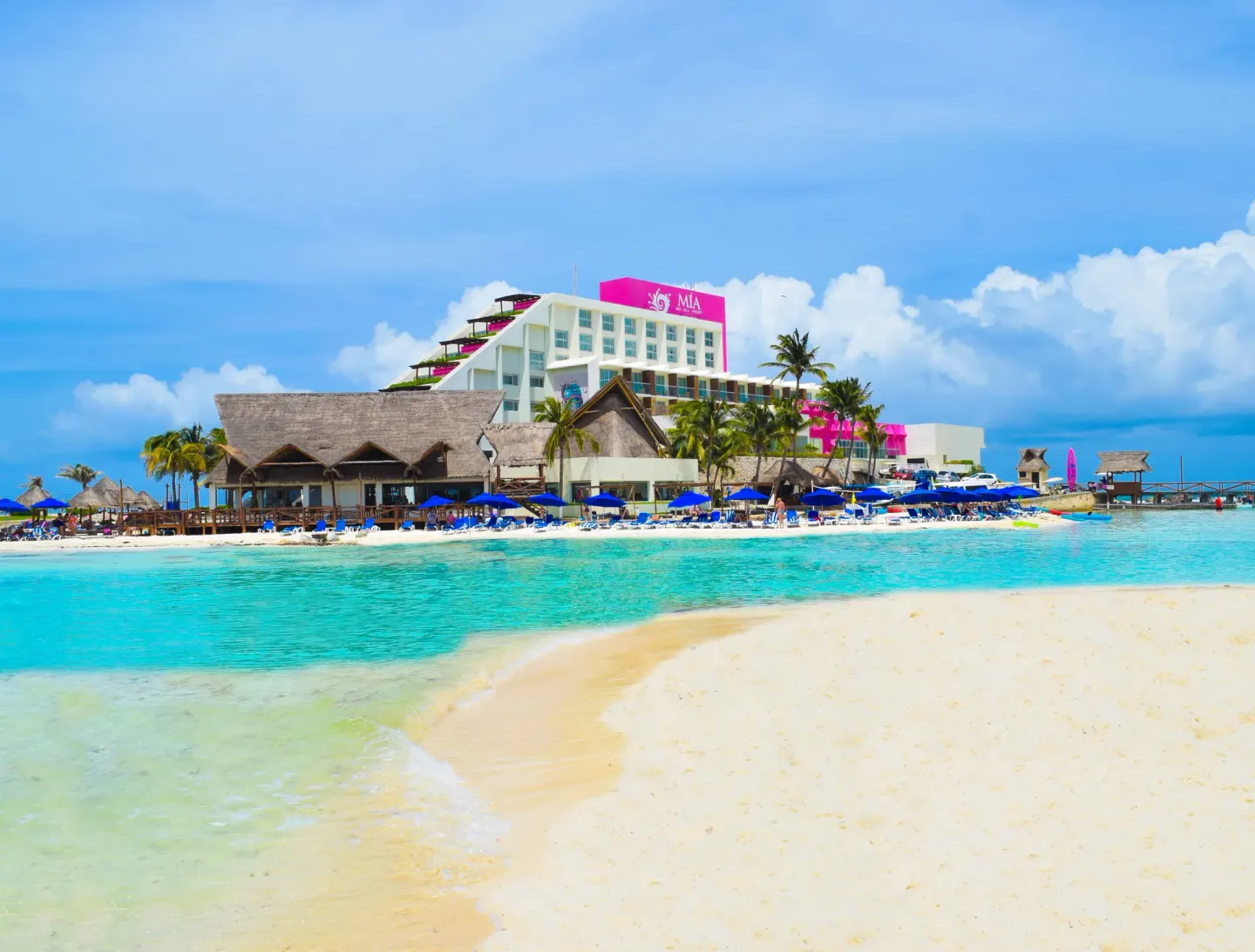 Resort beach with blue umbrellas, palapa roofs, and turquoise water at Mia Reef Isla Mujeres.