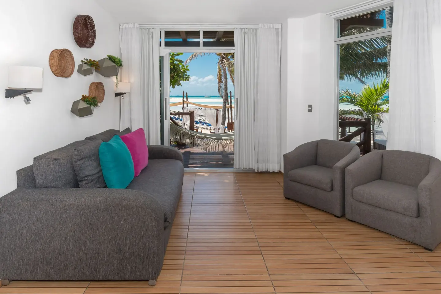 Sitting area at Mia Reef Isla Mujeres with gray sofas, armchairs, and beach views through glass doors.
