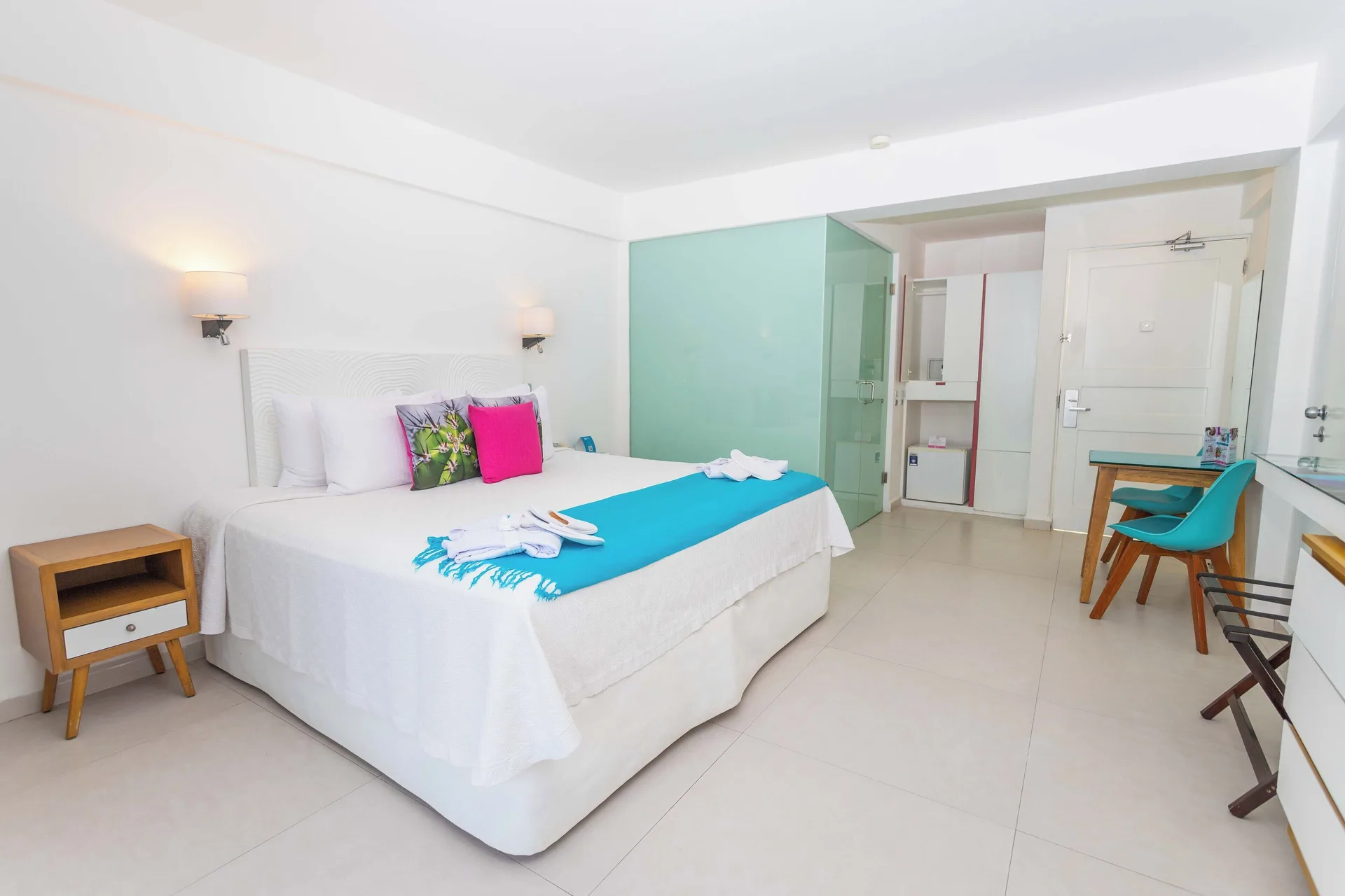 Guest room at Mia Reef Isla Mujeres with a king bed, turquoise runner, desk, and glass shower.