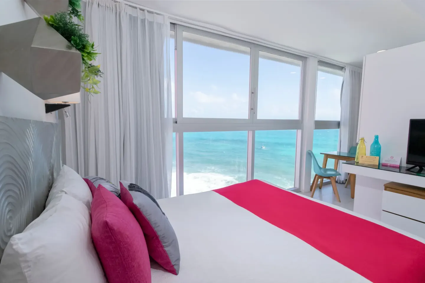 Ocean-view guest room at Mia Reef Isla Mujeres with white bedding and bright pink accents.