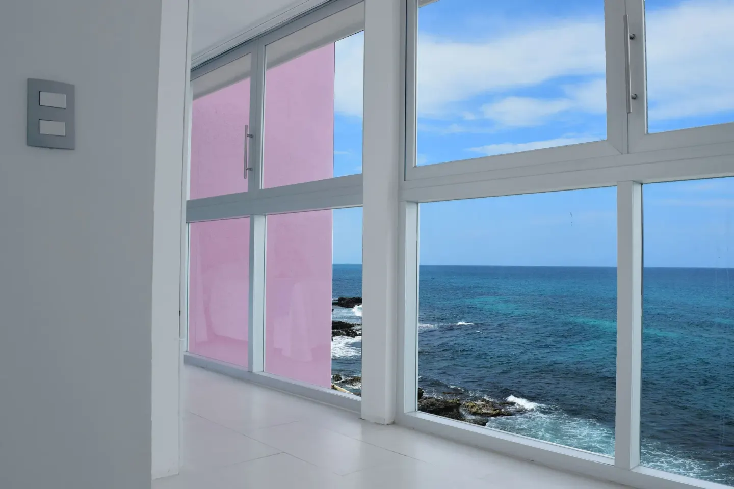 Large windows frame the ocean and rocky coast at Mia Reef Isla Mujeres.
