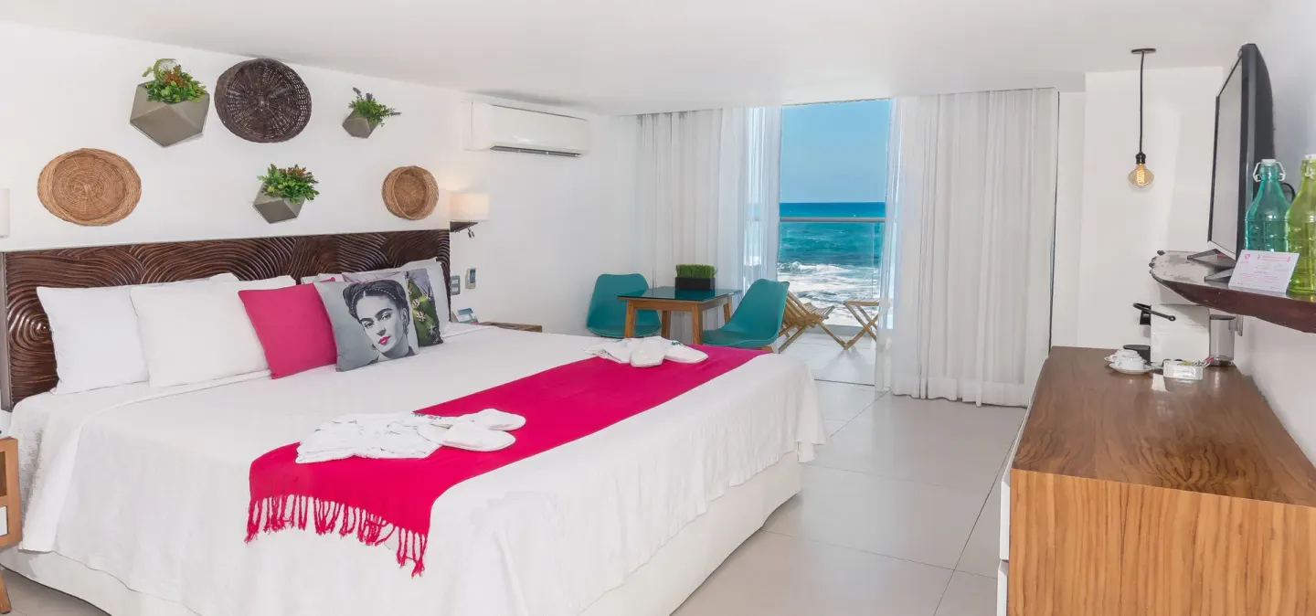 Oceanfront king bed guest room with white linens and turquoise seating at Mia Reef Isla Mujeres.
