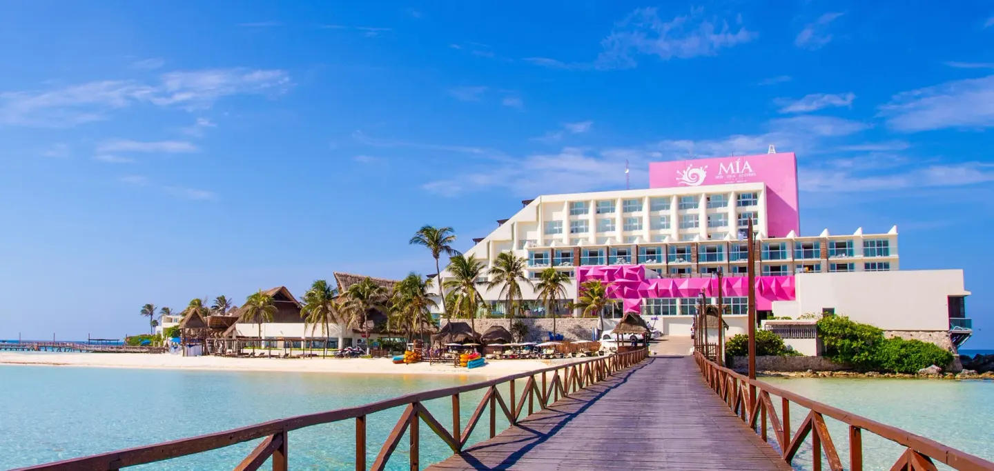 Resort exterior and wooden bridge over turquoise water at Mia Reef Isla Mujeres.