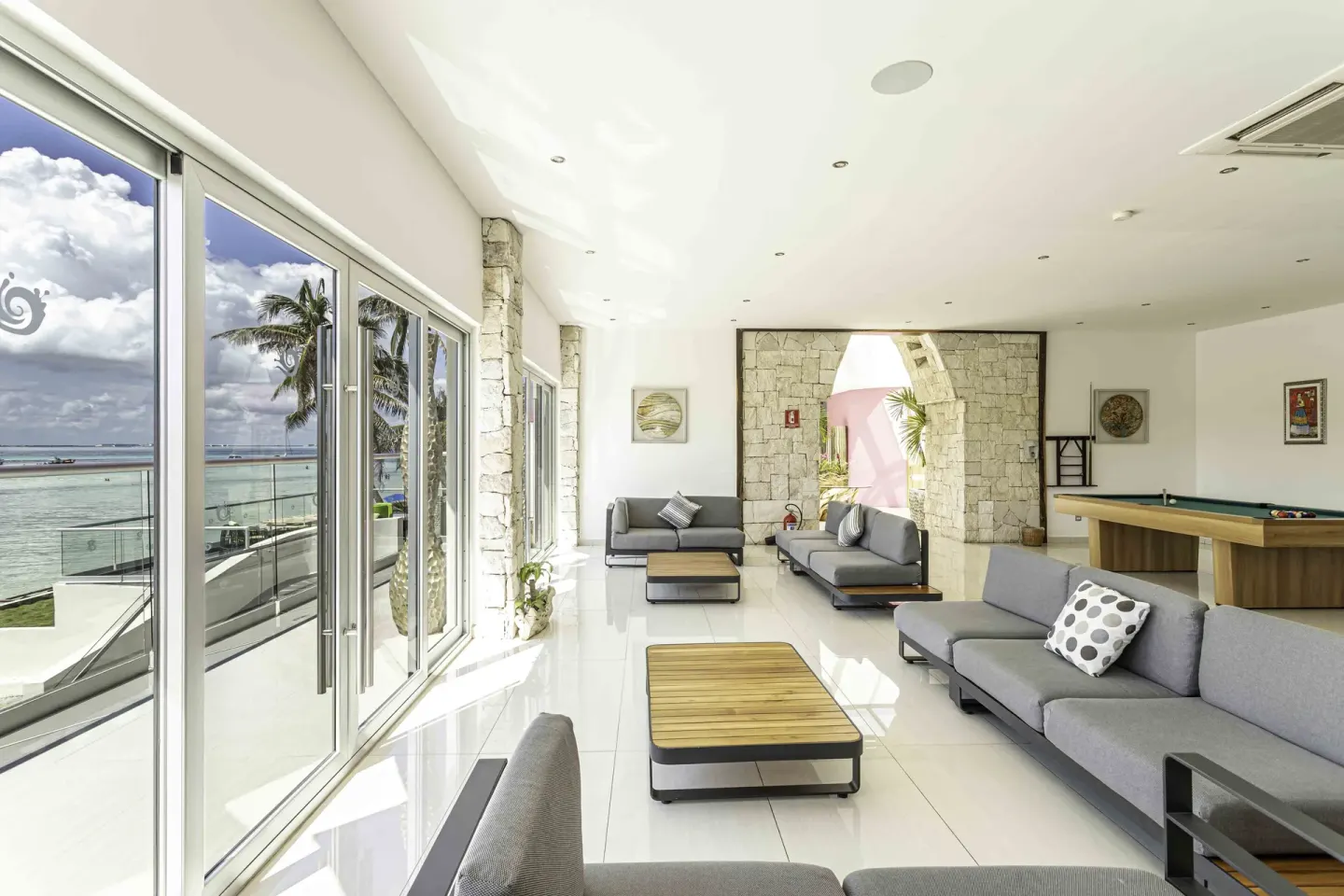 Bright lounge with sofas, billiards, and ocean-facing windows at Mia Reef Isla Mujeres.