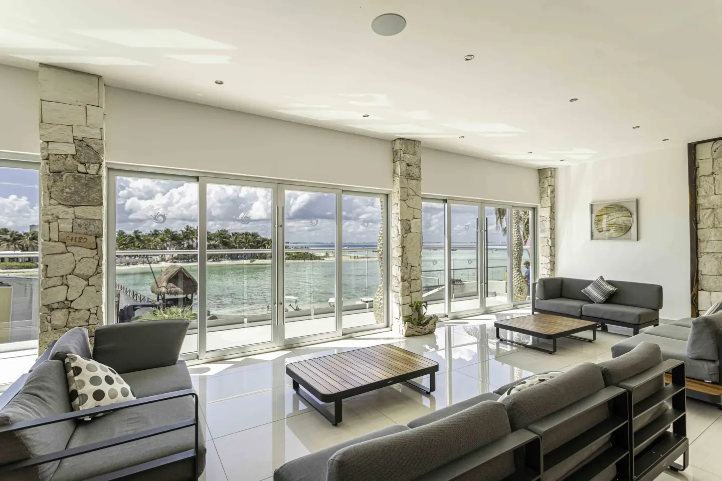 Bright lounge at Mia Reef Isla Mujeres with gray seating and floor-to-ceiling lagoon windows.