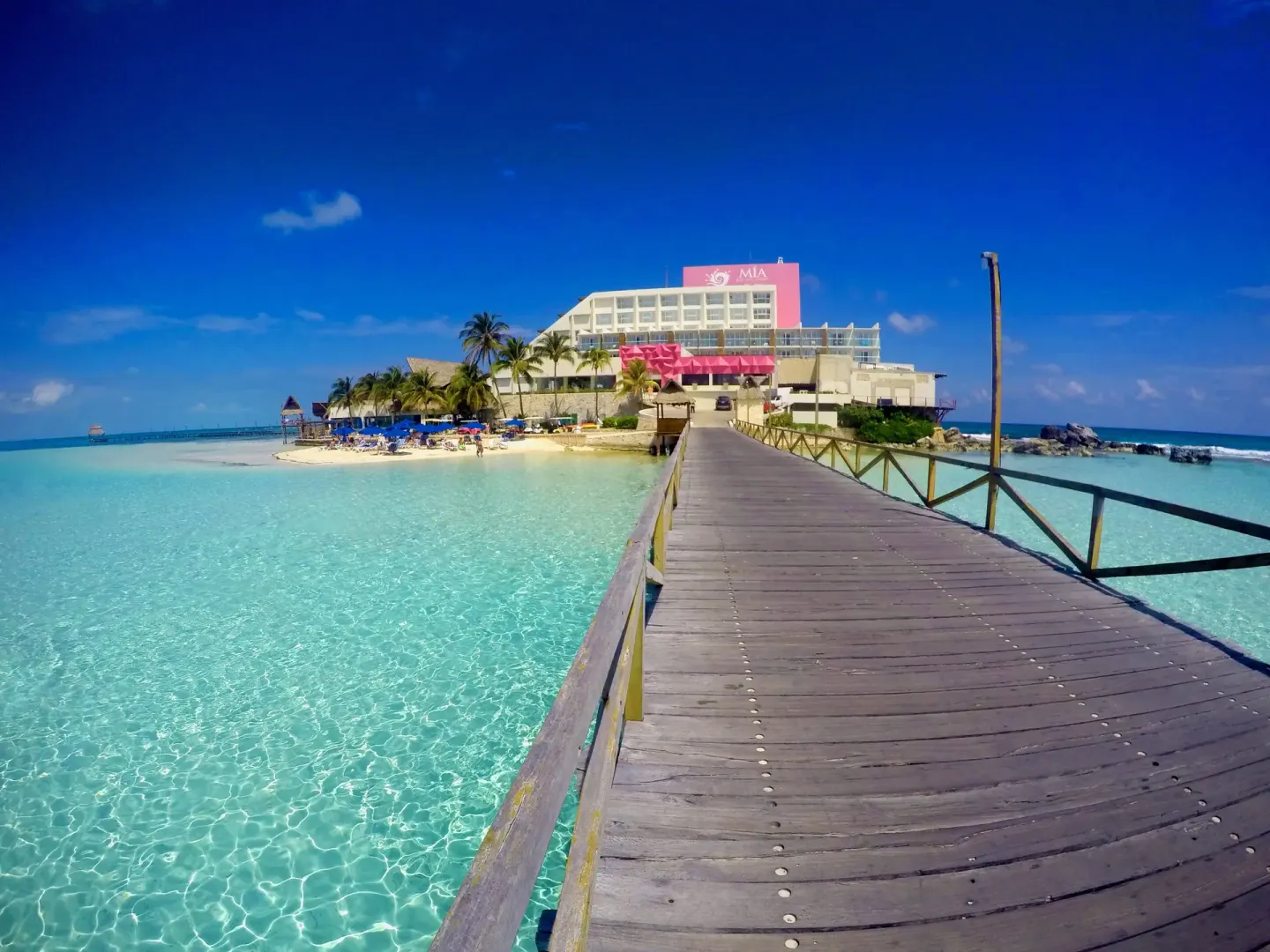 Wooden pier over clear turquoise water leading to Mia Reef Isla Mujeres.