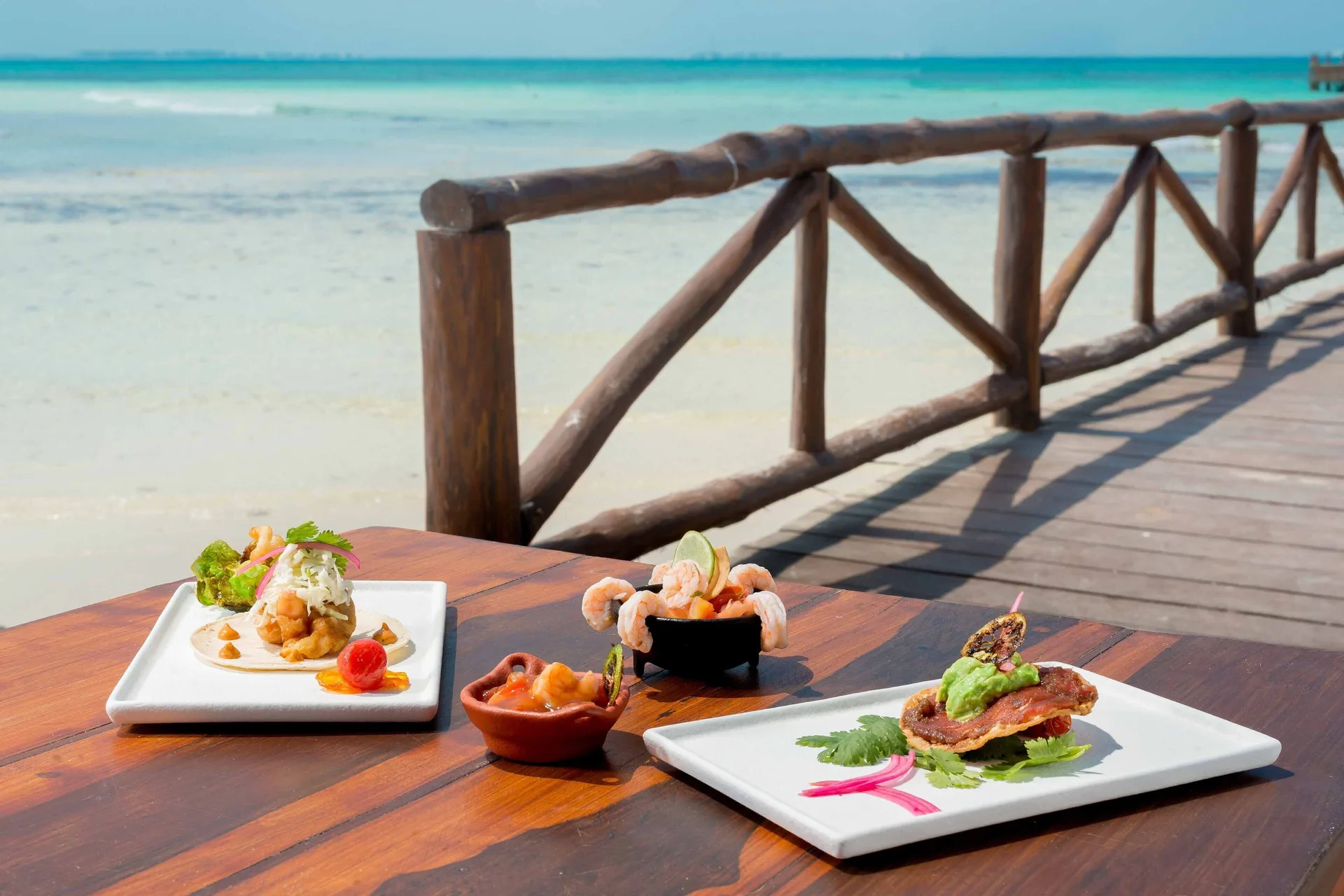 Plated seafood dishes sit on a waterfront table at Mia Reef Isla Mujeres.