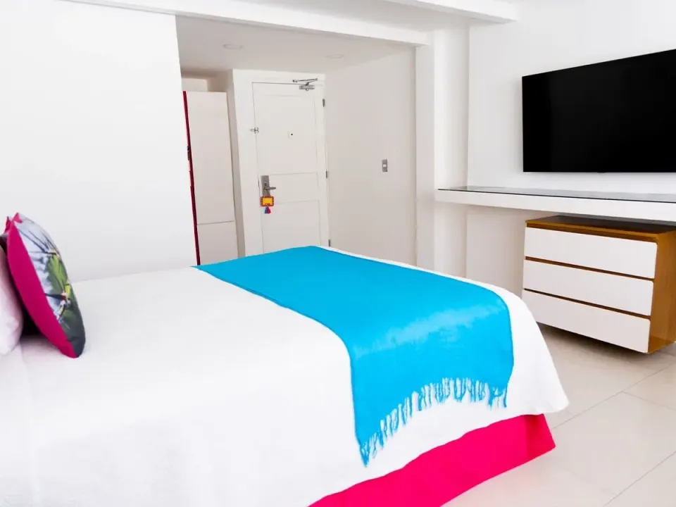 Basic Room bed with blue runner facing TV and entry door at Mia Reef Isla Mujeres.