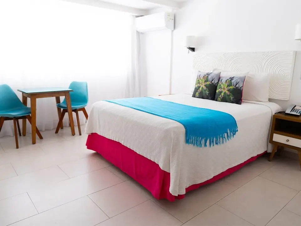 Basic Room bed with blue runner and window-side table at Mia Reef Isla Mujeres.